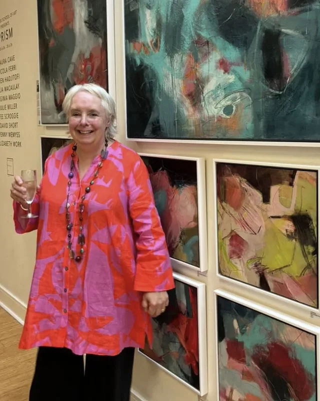 Julie Miller standing in a gallery beside a group of her framed abstract paintings.